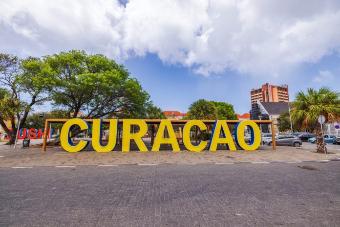 Large,Yellow,Curacao,Sign,Displayed,Outdoors,With,Trees,,Buildings,,And